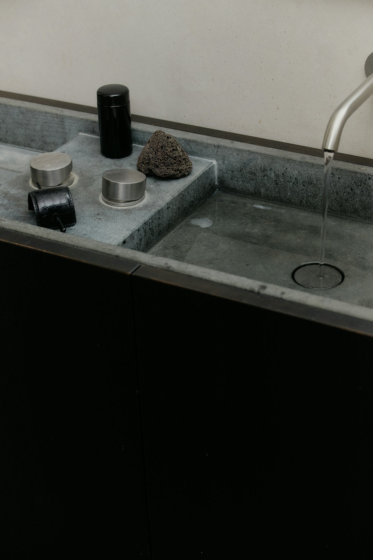 Photograph of a stone bathroom counter with beautiful, black, minimalist accessories and bath apothecary items