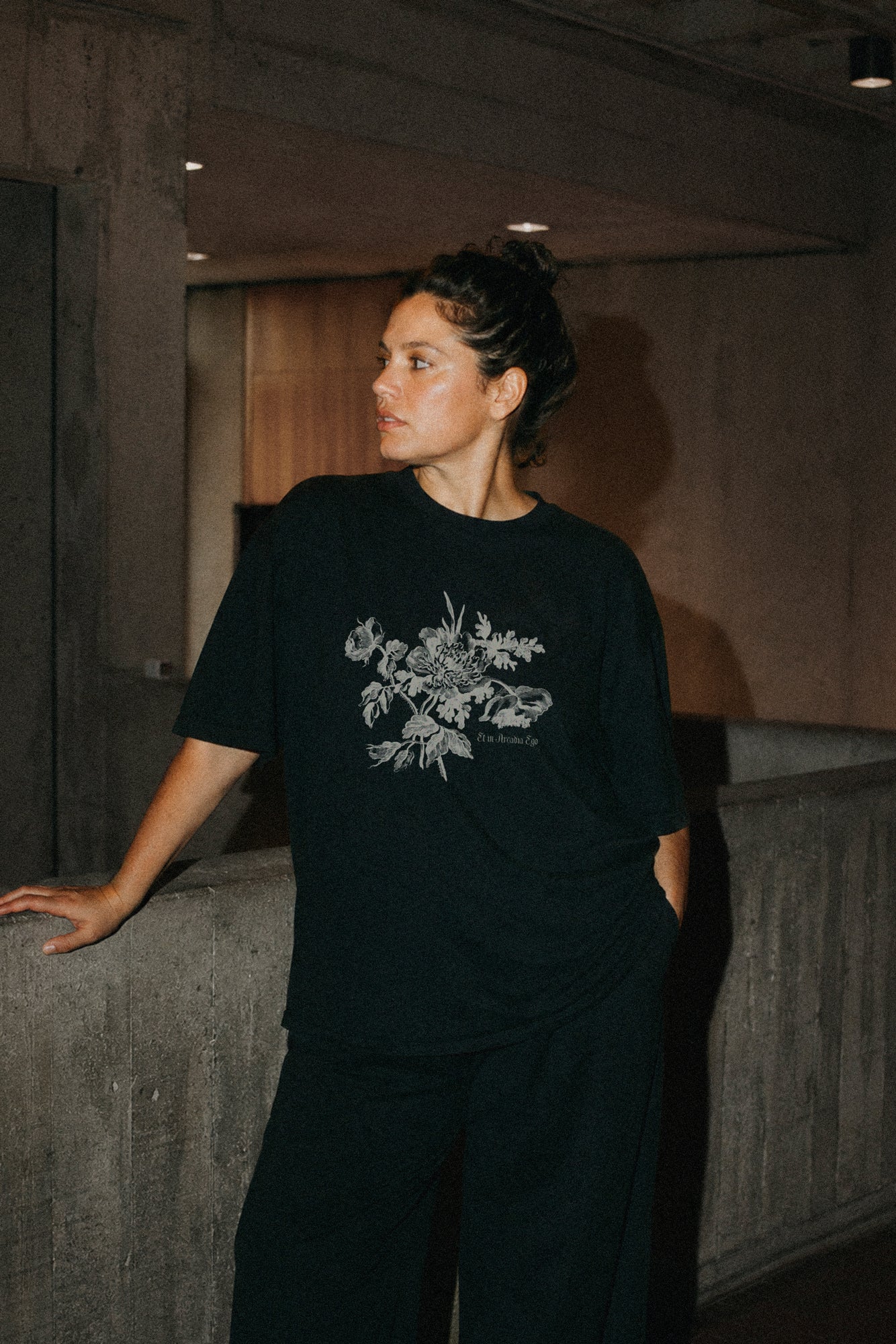 Person wearing a black t-shirt with a floral design and the quote "et in arcadia ego" in an indoor setting