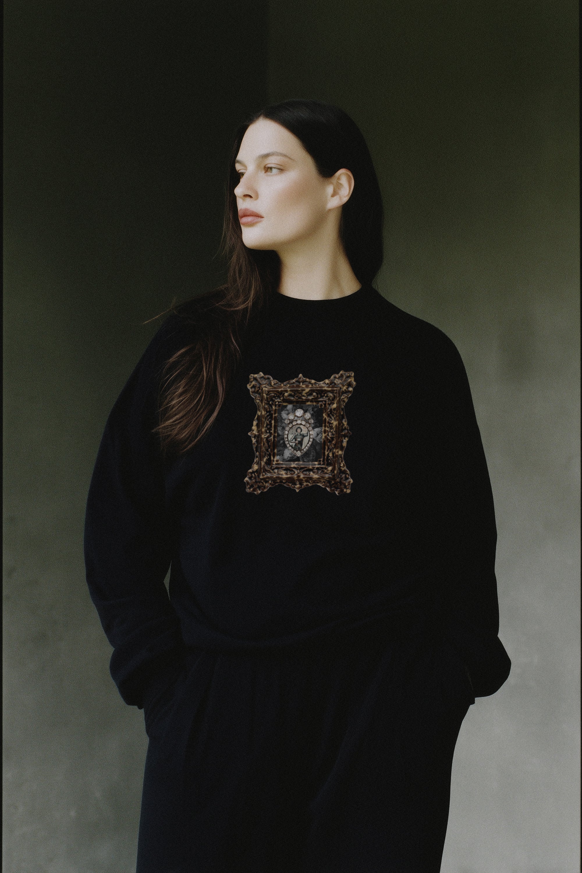 Woman wearing a black sweater with a decorative emblem against a dark background