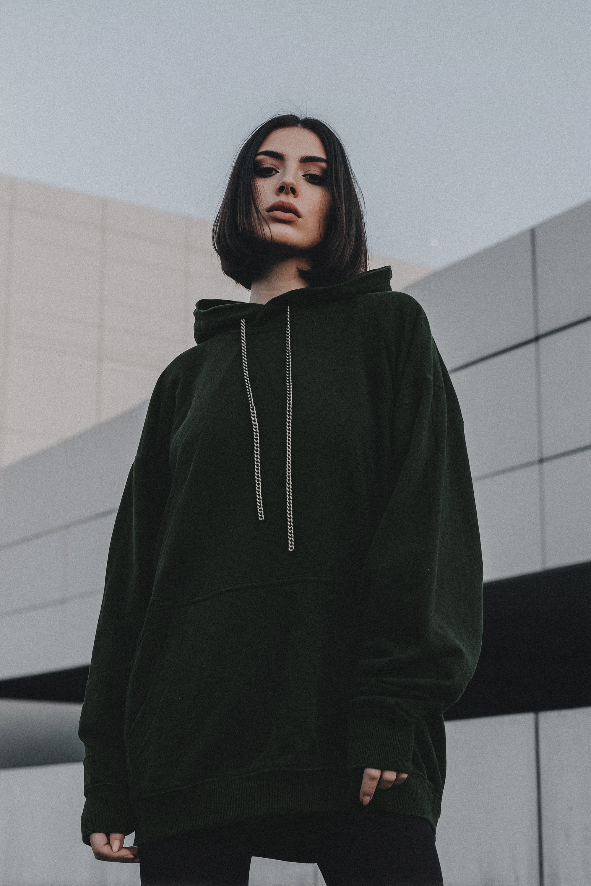 Person wearing a dark green hoodie standing in front of a modern building.