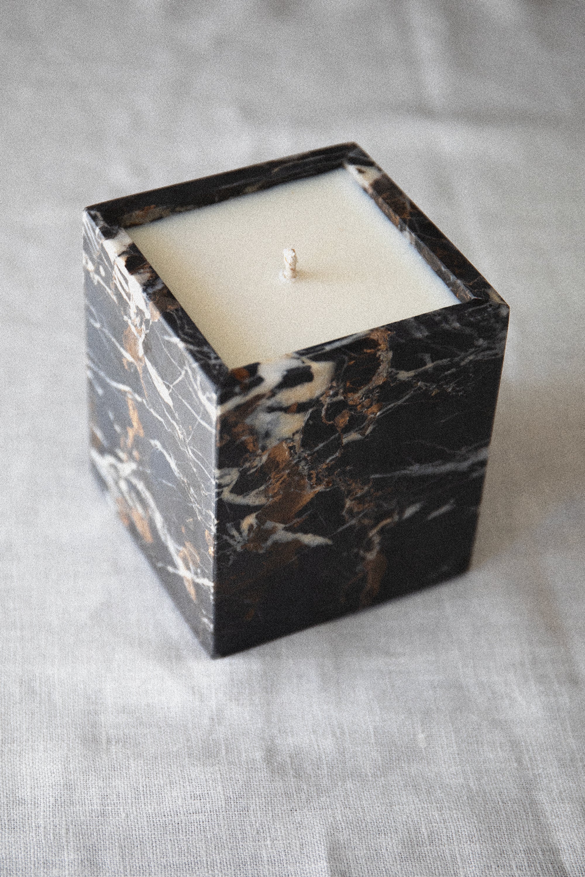 Candle in a black marble-textured container on a light gray fabric background