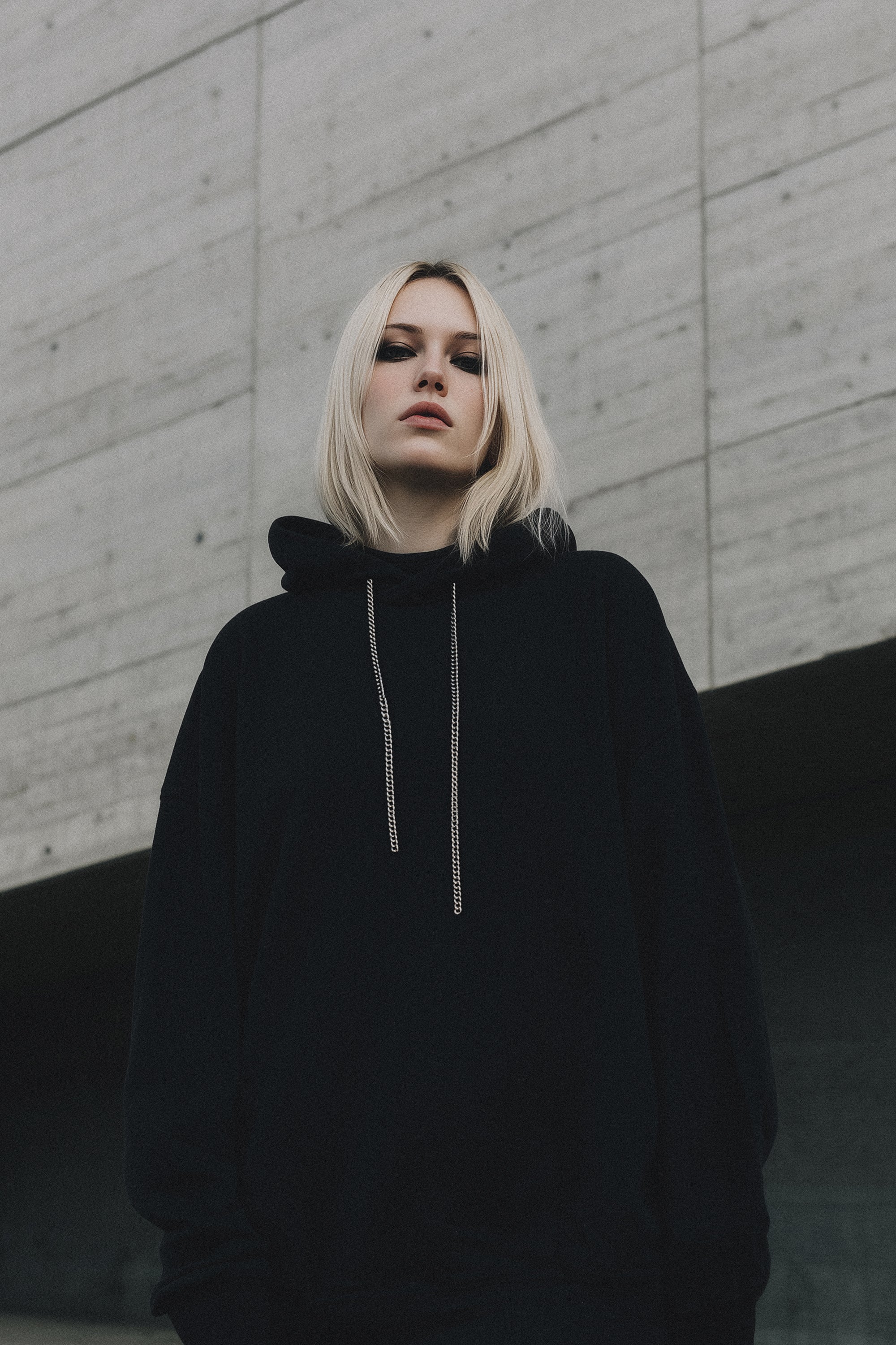 Person wearing a black hoodie against a concrete wall