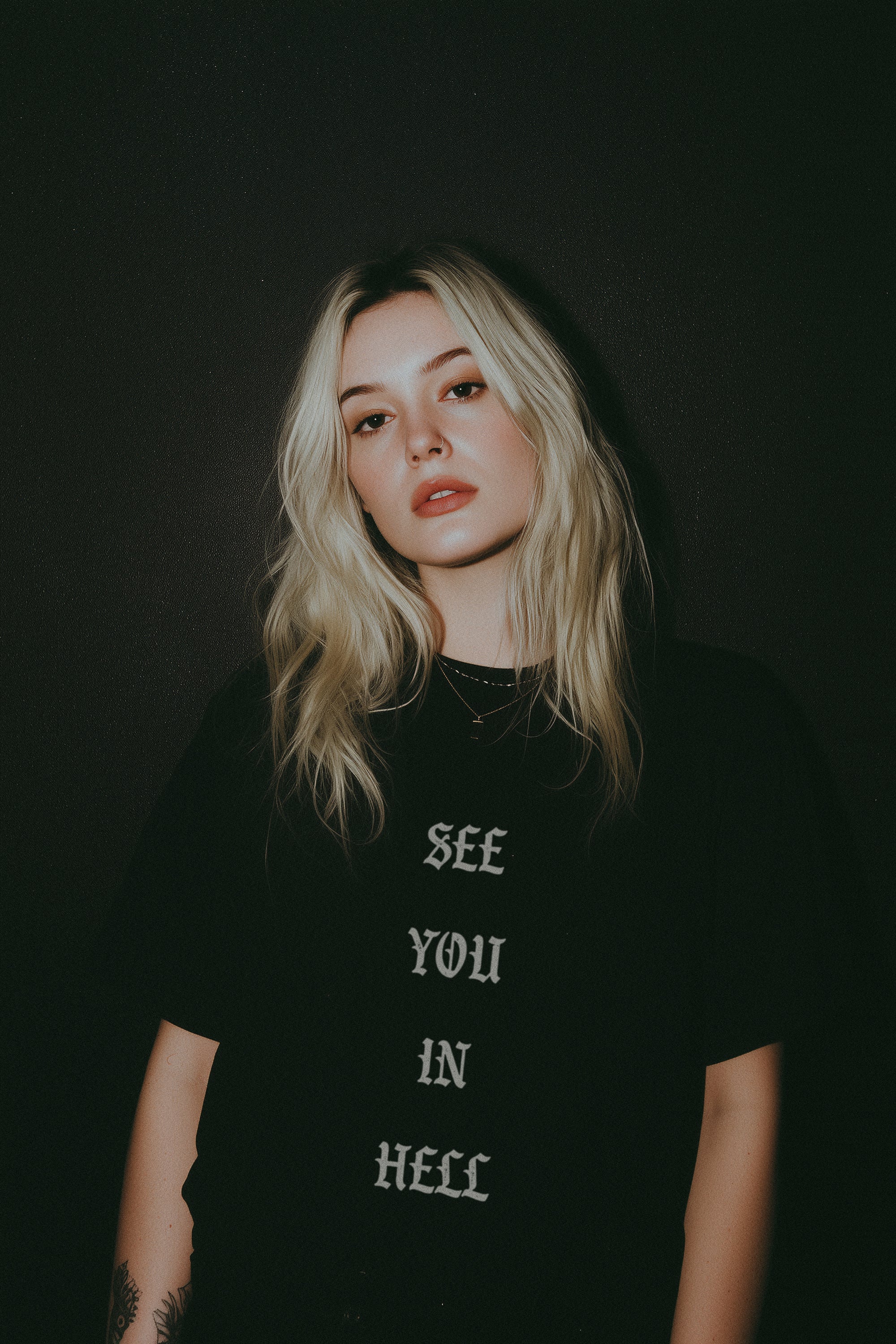 Person wearing a black t-shirt that reads See You in Hell in a gothic design against a dark background