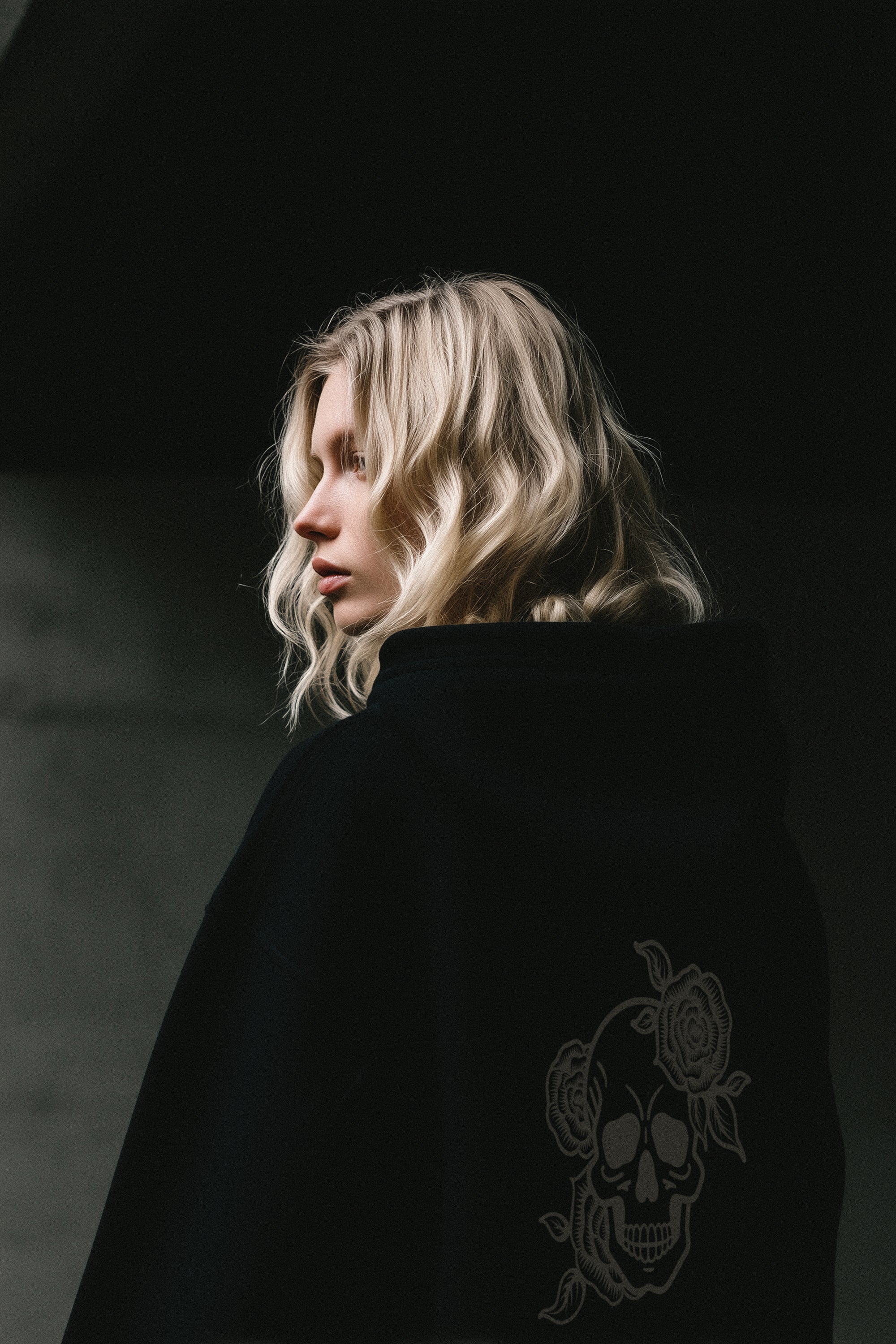 Person wearing a black hooded sweatshirt with a skull design on a dark background